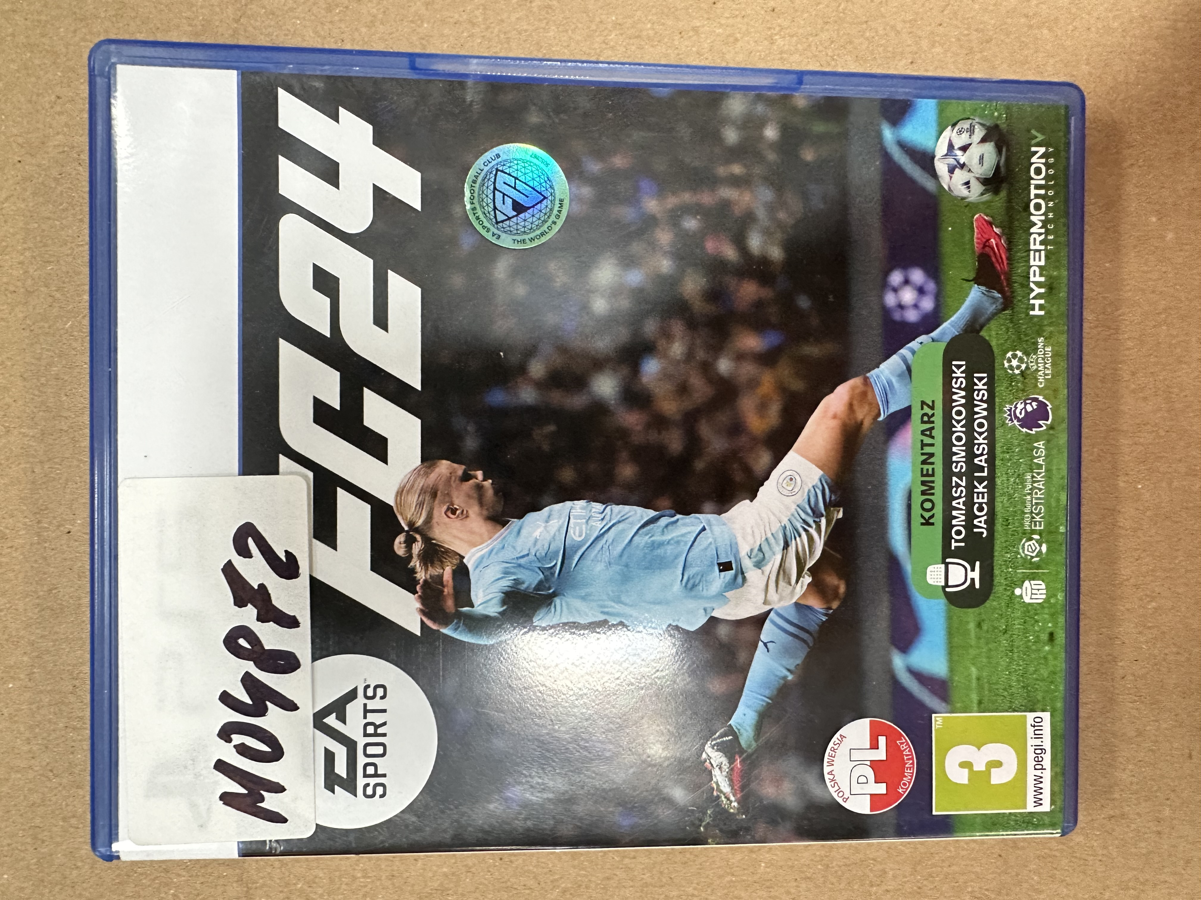 Pudełko gry wideo FIFA 24 z piłkarzem. Pudełko leży na stole.