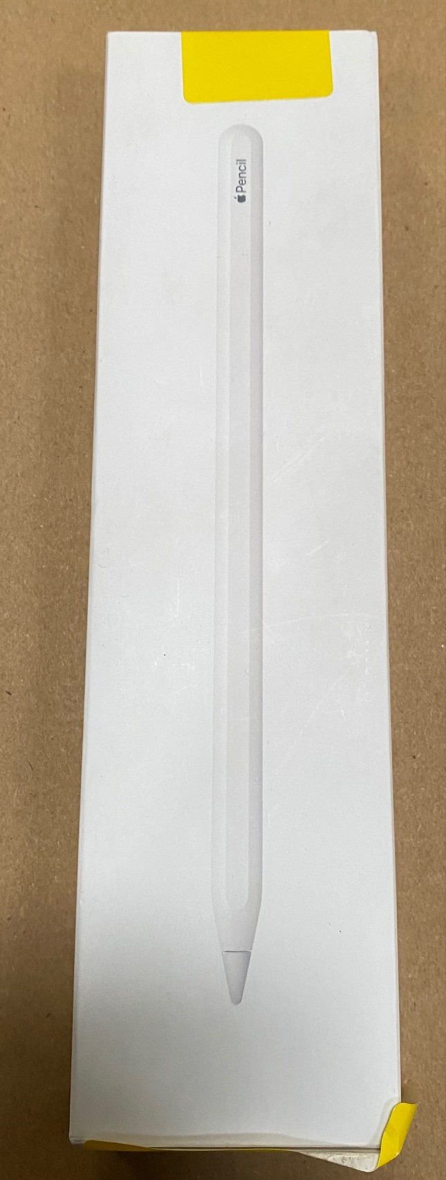 Białe pudełko z Apple Pencil w środku. Żółta naklejka na górze.