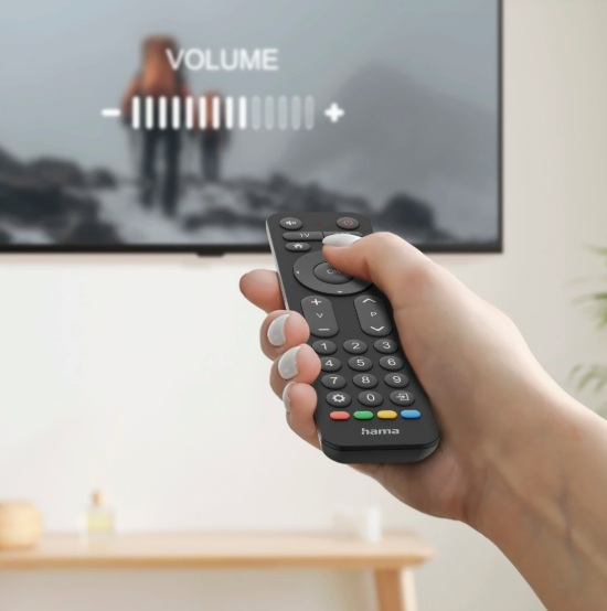 Ręka trzyma pilota skierowanego w stronę telewizora. Telewizor wyświetla pasek głośności.