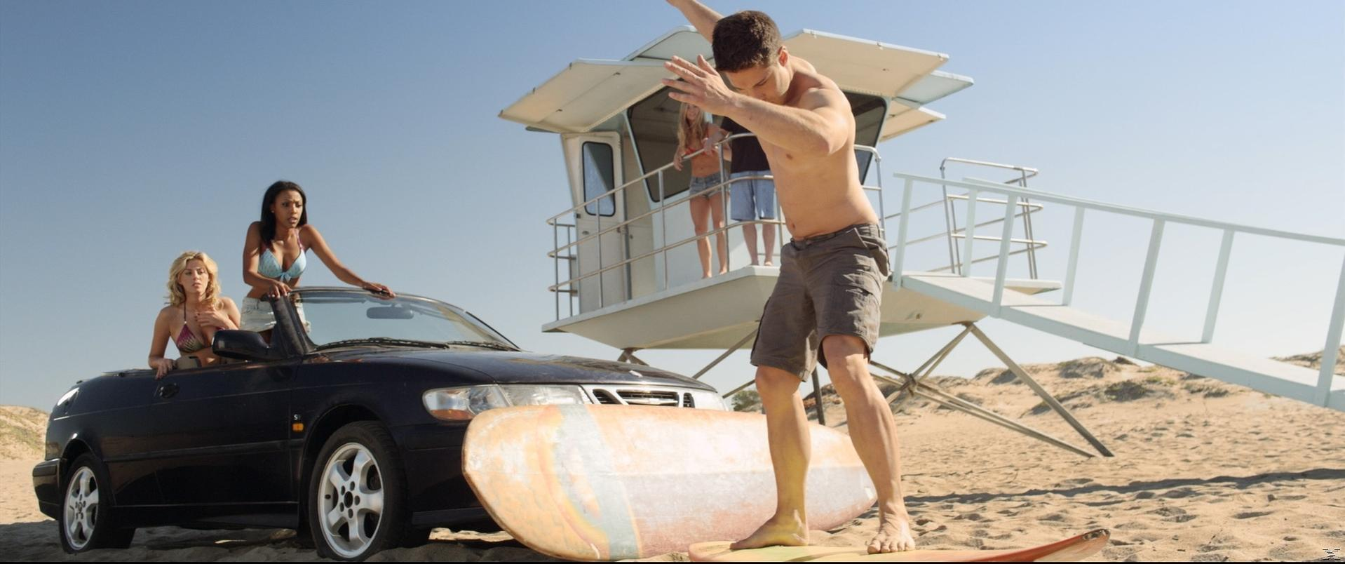 Menschen am Strand mit einem Auto und einem Rettungsturm. Ein Mann ist kurz vorm Surfen.