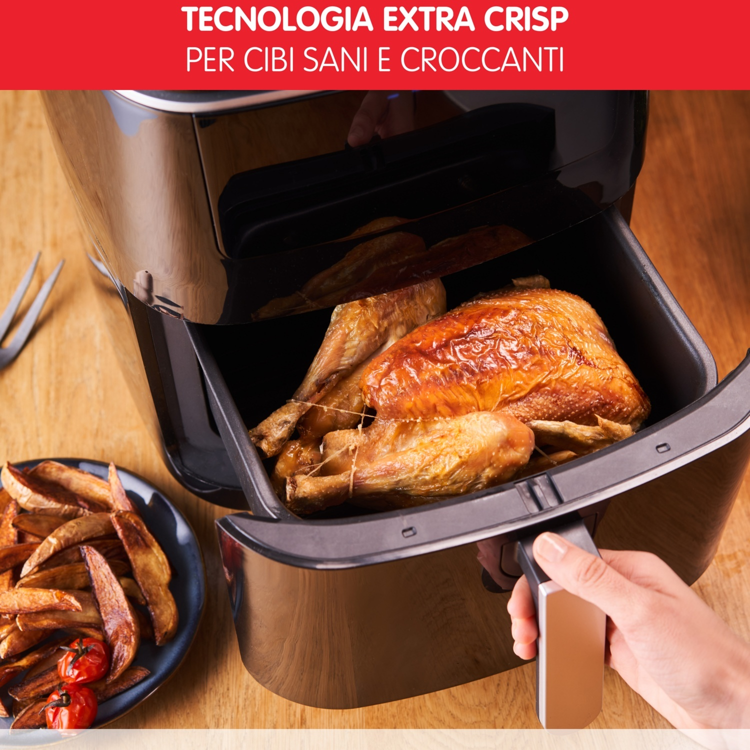 Friggitrice ad aria con pollo cotto all'interno. Mano apre il cassetto. Sfondo: superficie in legno.