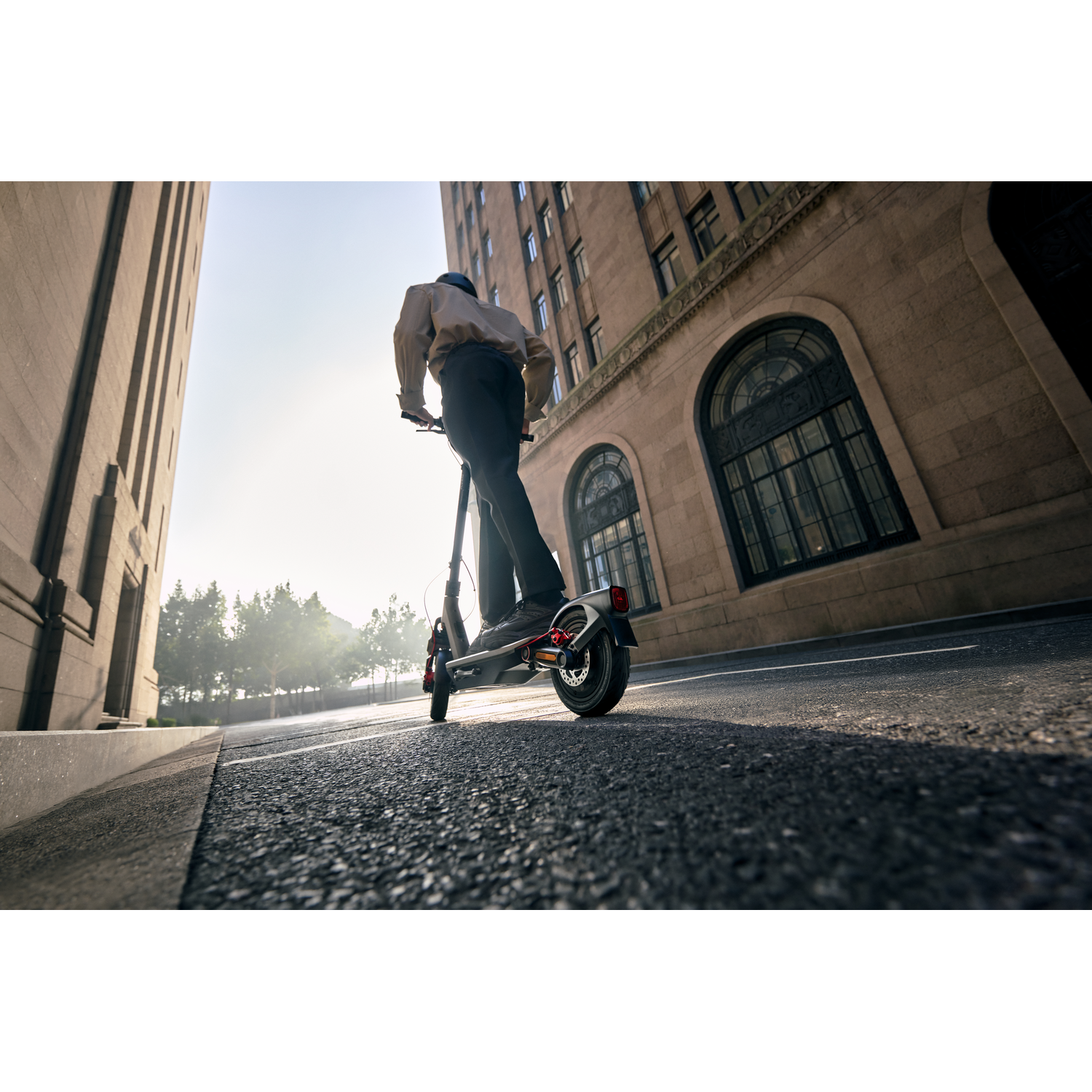 A person on a scooter rides down a street between buildings.