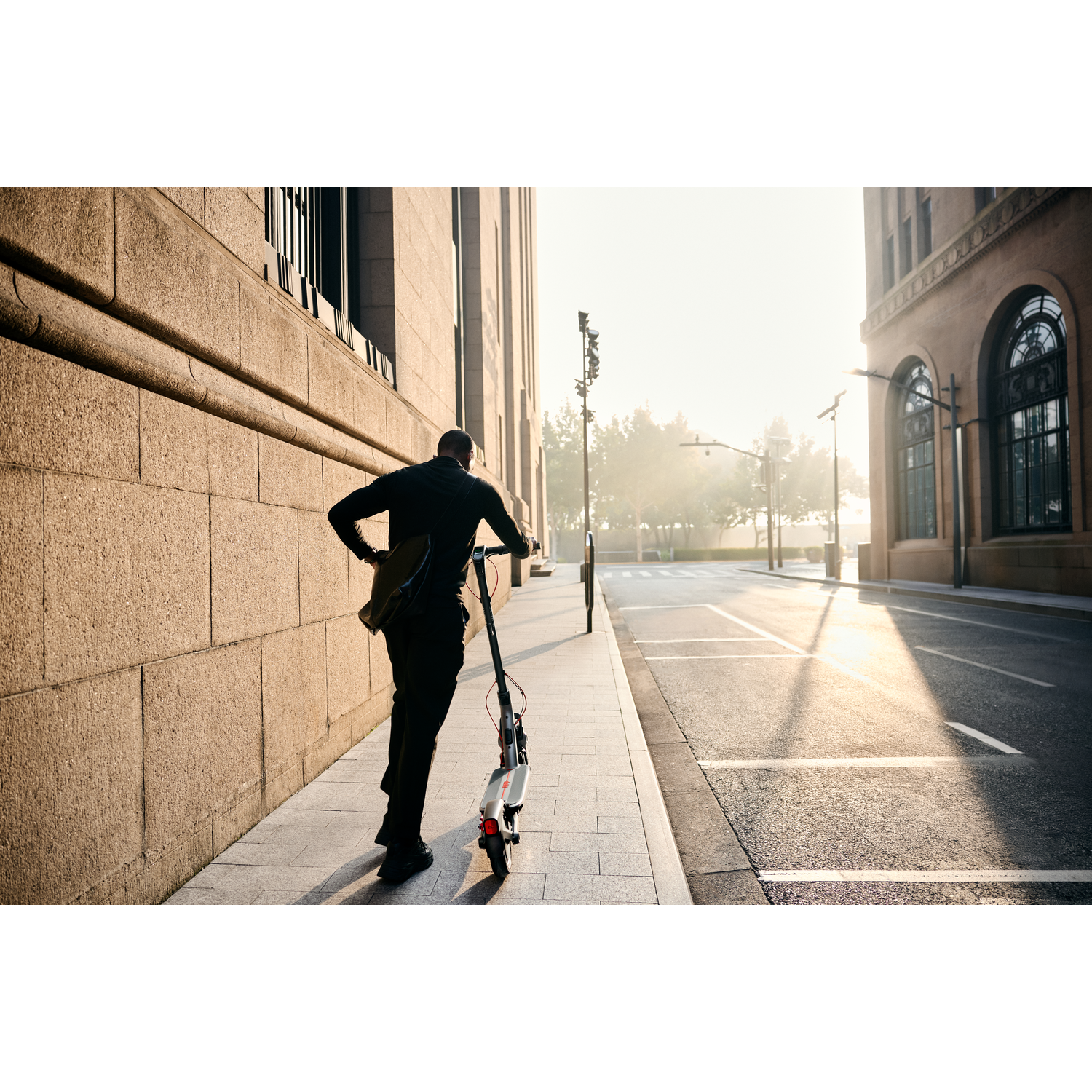 A man walks on a sidewalk next to a building, holding a bag.