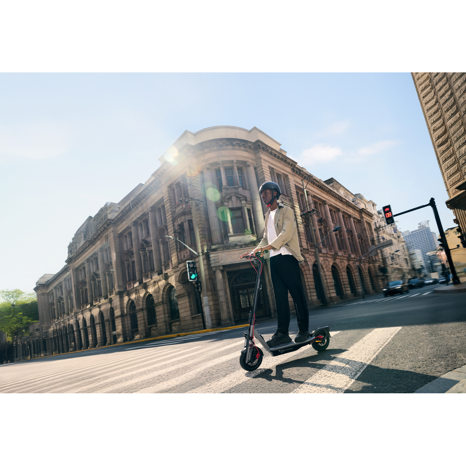 A person on an electric scooter on a city street, with a building and sun in the background.