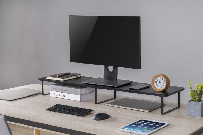 Asztal számítógép monitorral, könyvekkel, billentyűzettel, tablettel, órával és egy kis növénnyel.