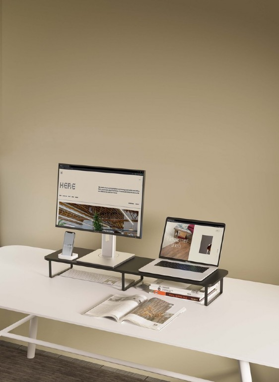 Asztal monitorral, laptop, okostelefon és könyvekkel egy állványon. Semleges háttér.
