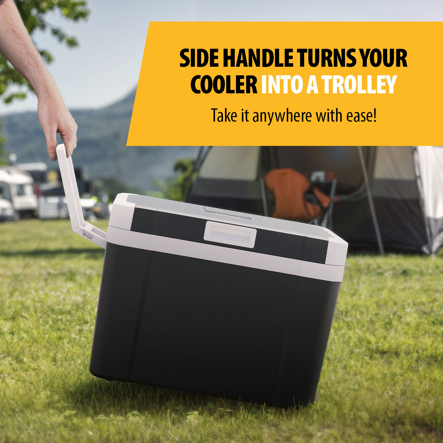 A black cooler with a white handle being pulled by a hand. The cooler is on grass, with a campsite background.