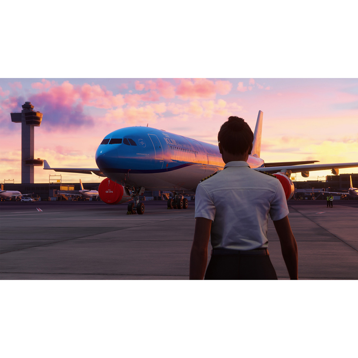 Una persona mira un avión azul en una pista, con una torre y un cielo de atardecer de fondo.