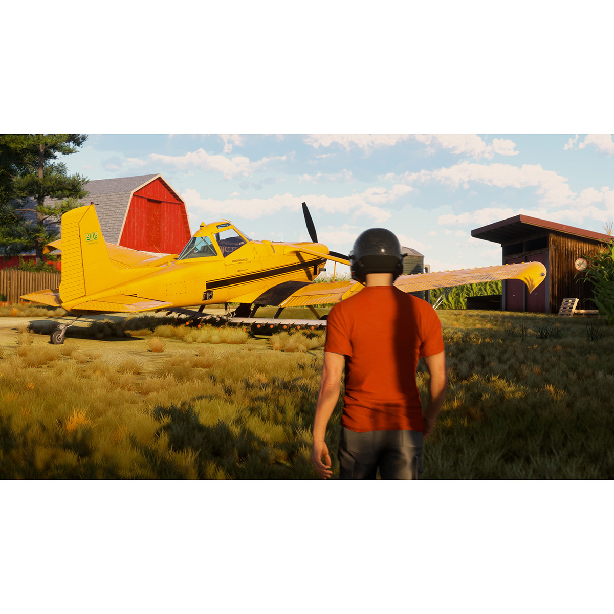 Avión fumigador amarillo en un campo de hierba cerca de un granero rojo. Una persona está de pie.