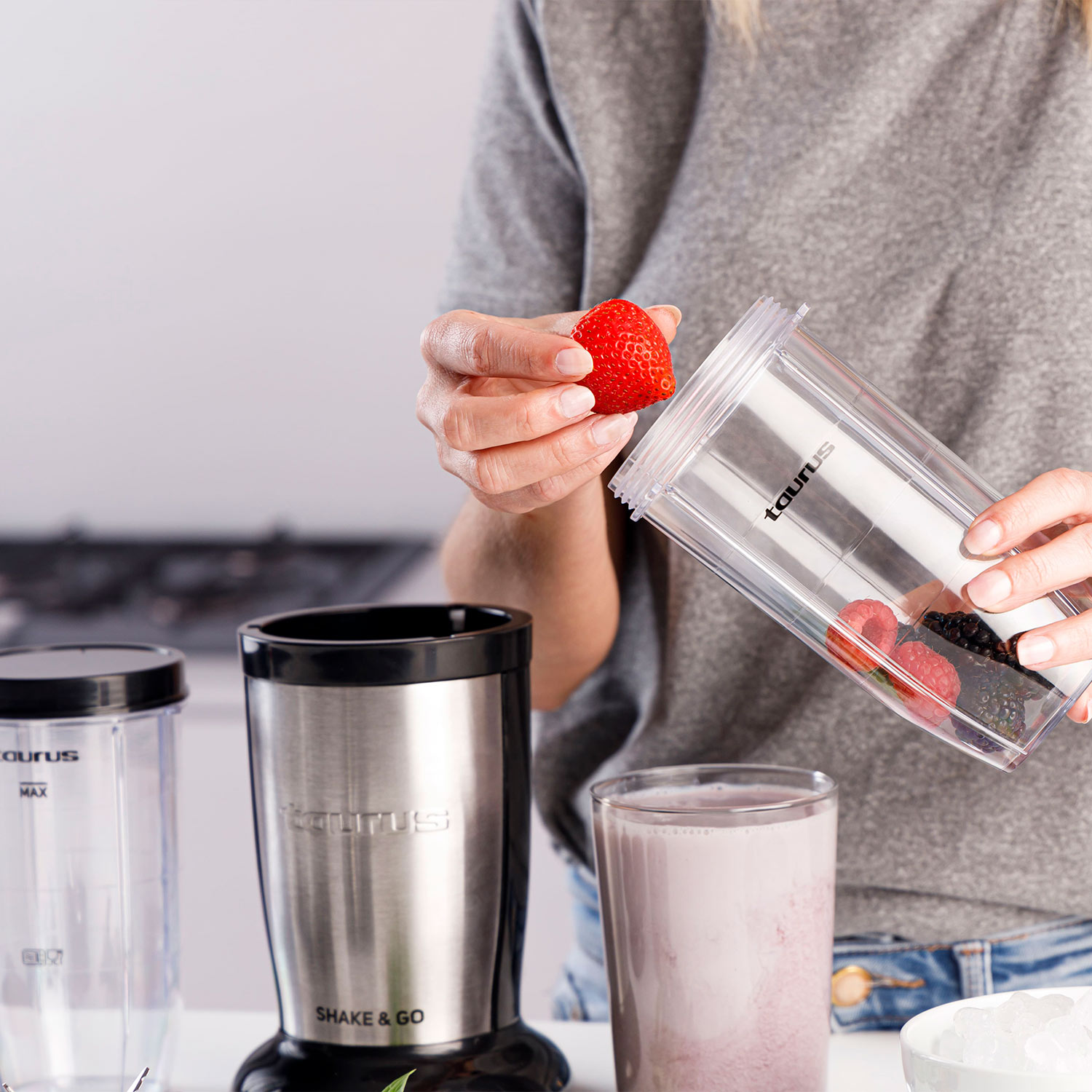 Una mujer vierte fresas en una licuadora con otros ingredientes.