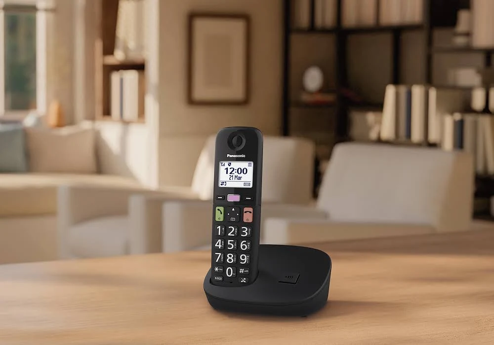 Teléfono inalámbrico Panasonic negro en su base, sobre una mesa de madera.