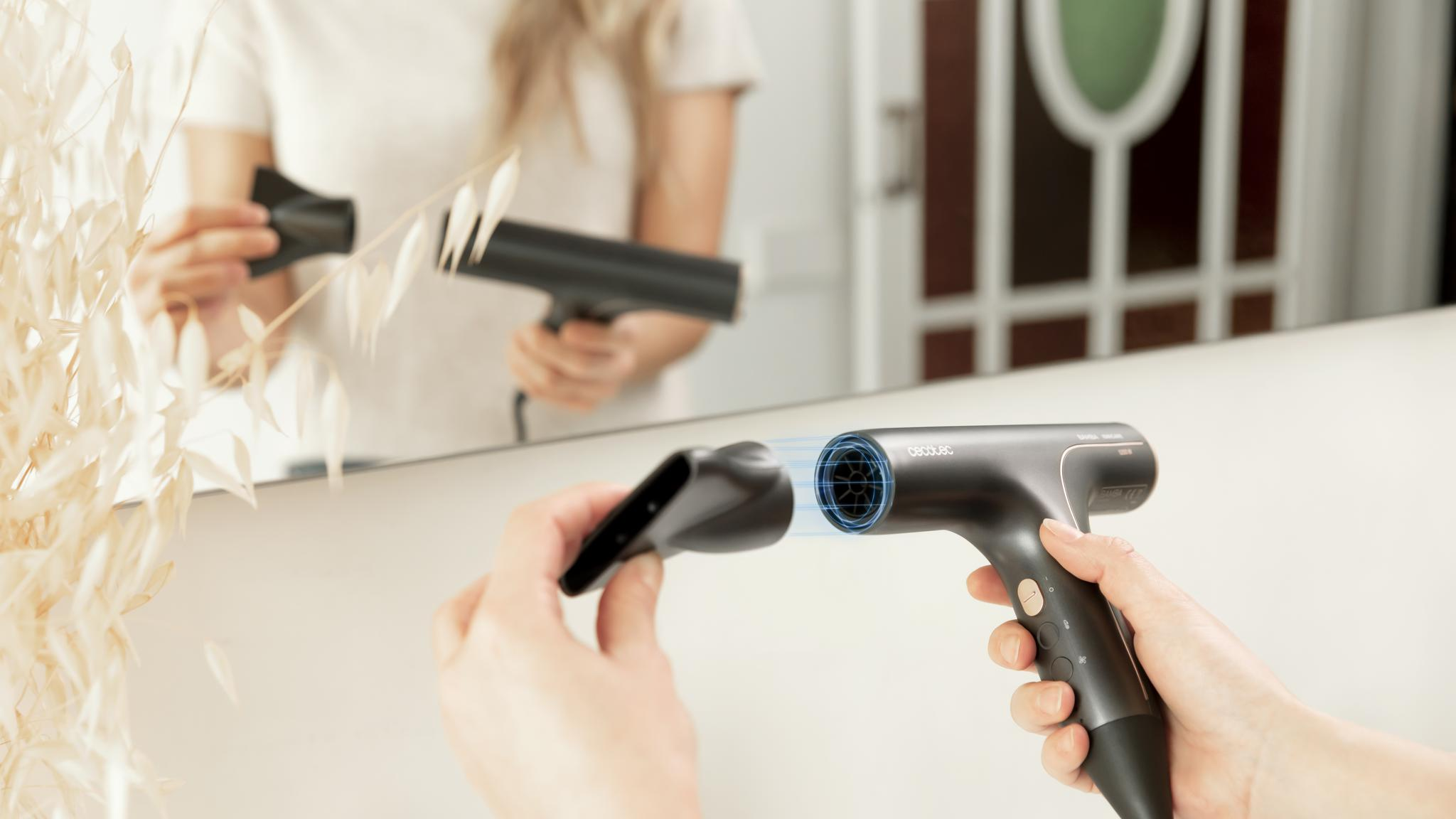 Kobieta trzyma czarną suszarkę do włosów z nasadką przed lustrem.