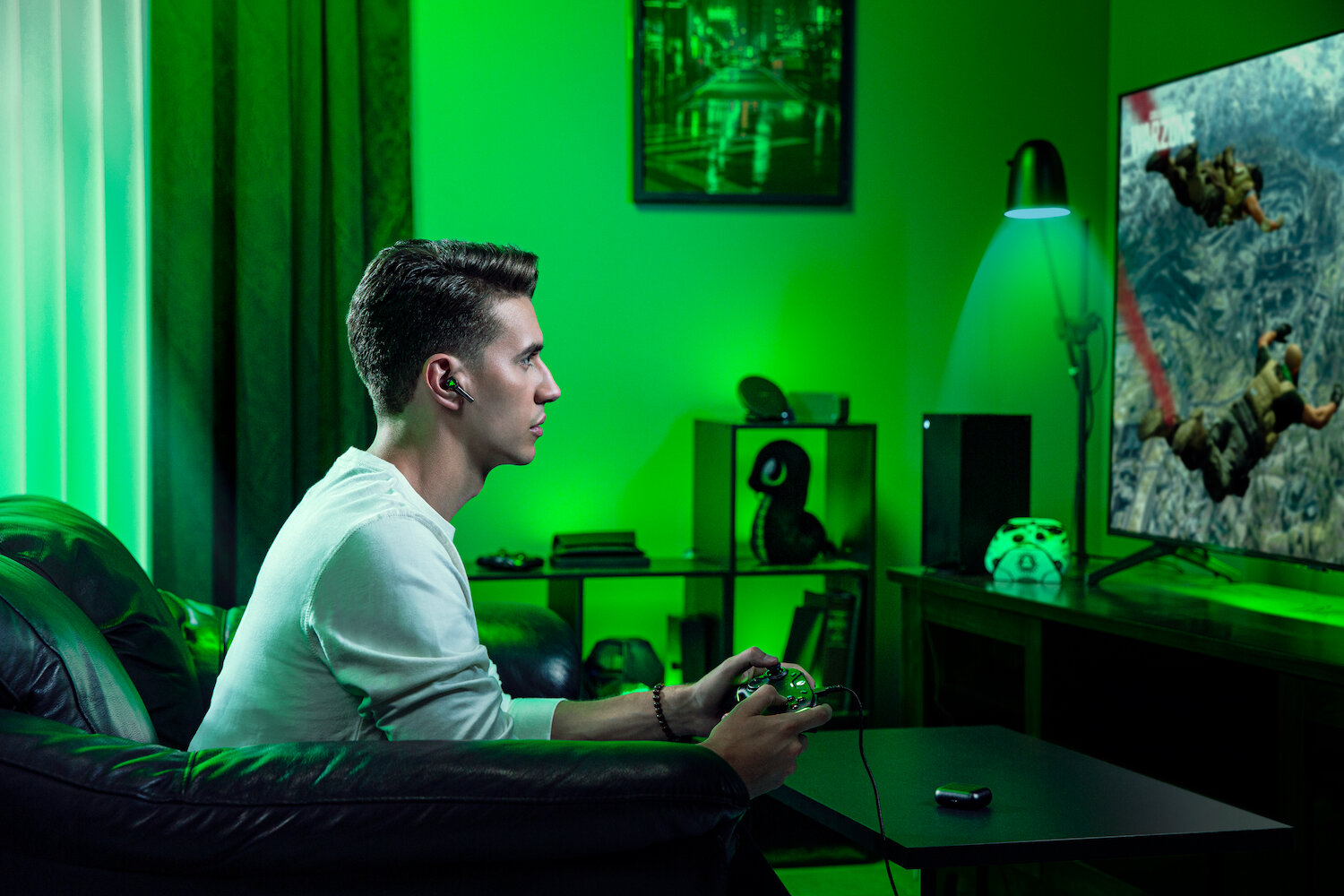 Mężczyzna w białej koszuli gra w grę wideo. Duży telewizor wyświetla grę. Zielone oświetlenie oświetla pokój.