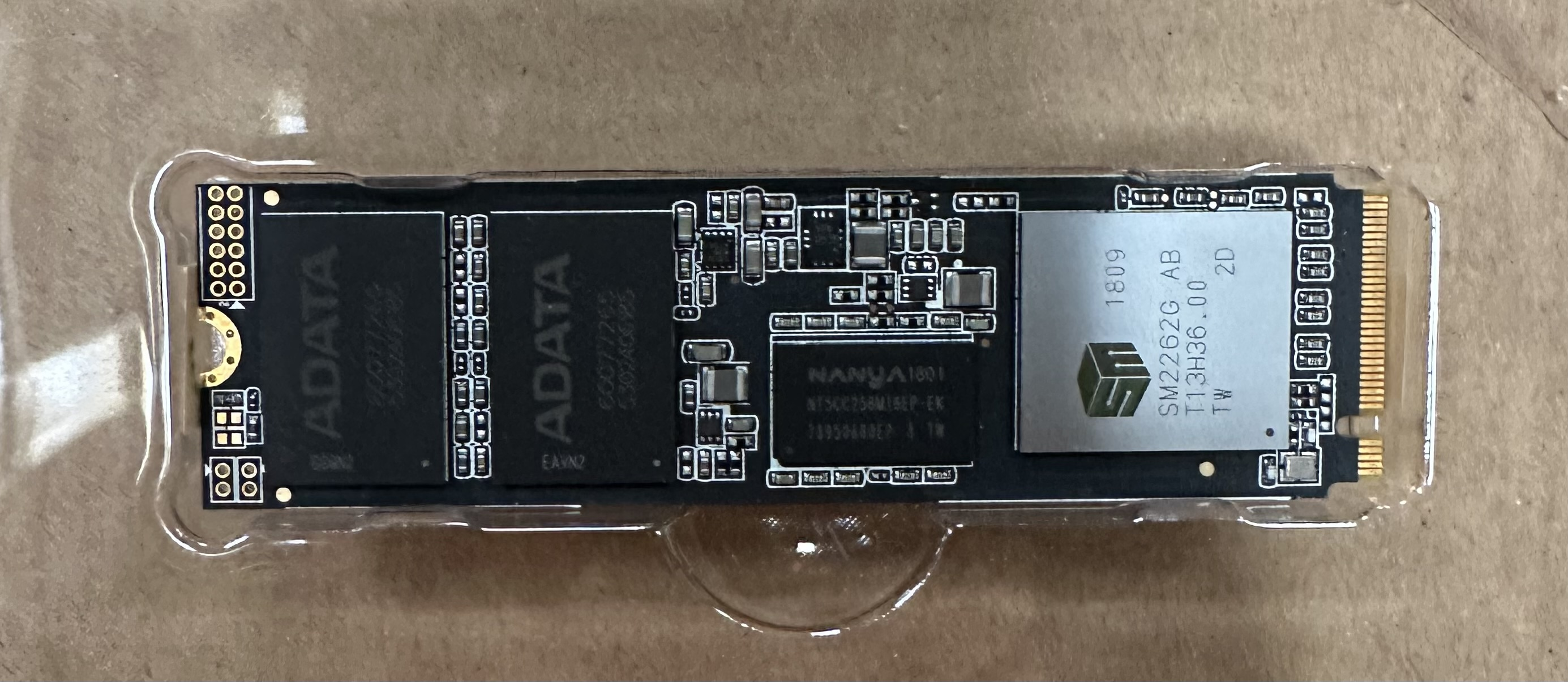 ADATA SSD w plastikowej obudowie. Czarna płytka z układami. Brązowe tło.