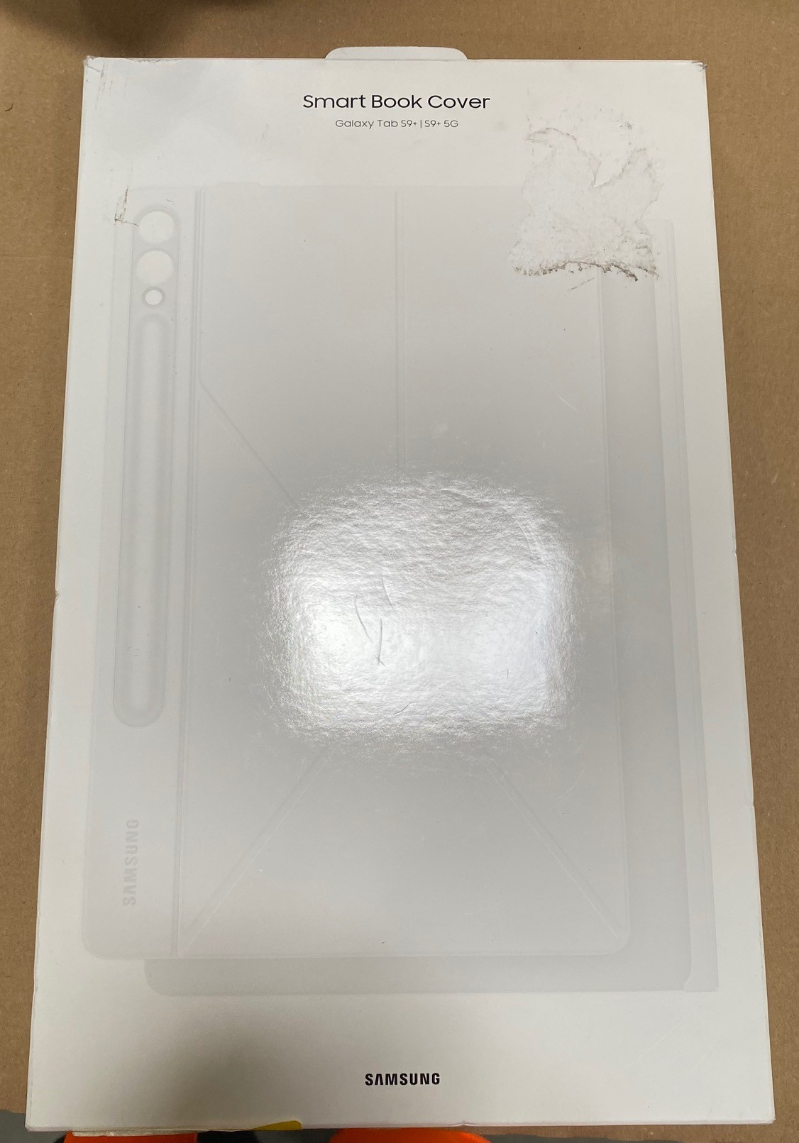 Białe pudełko z pokrywą z napisem 'Smart Book Cover' dla Galaxy Tab S9. Na brązowej powierzchni.