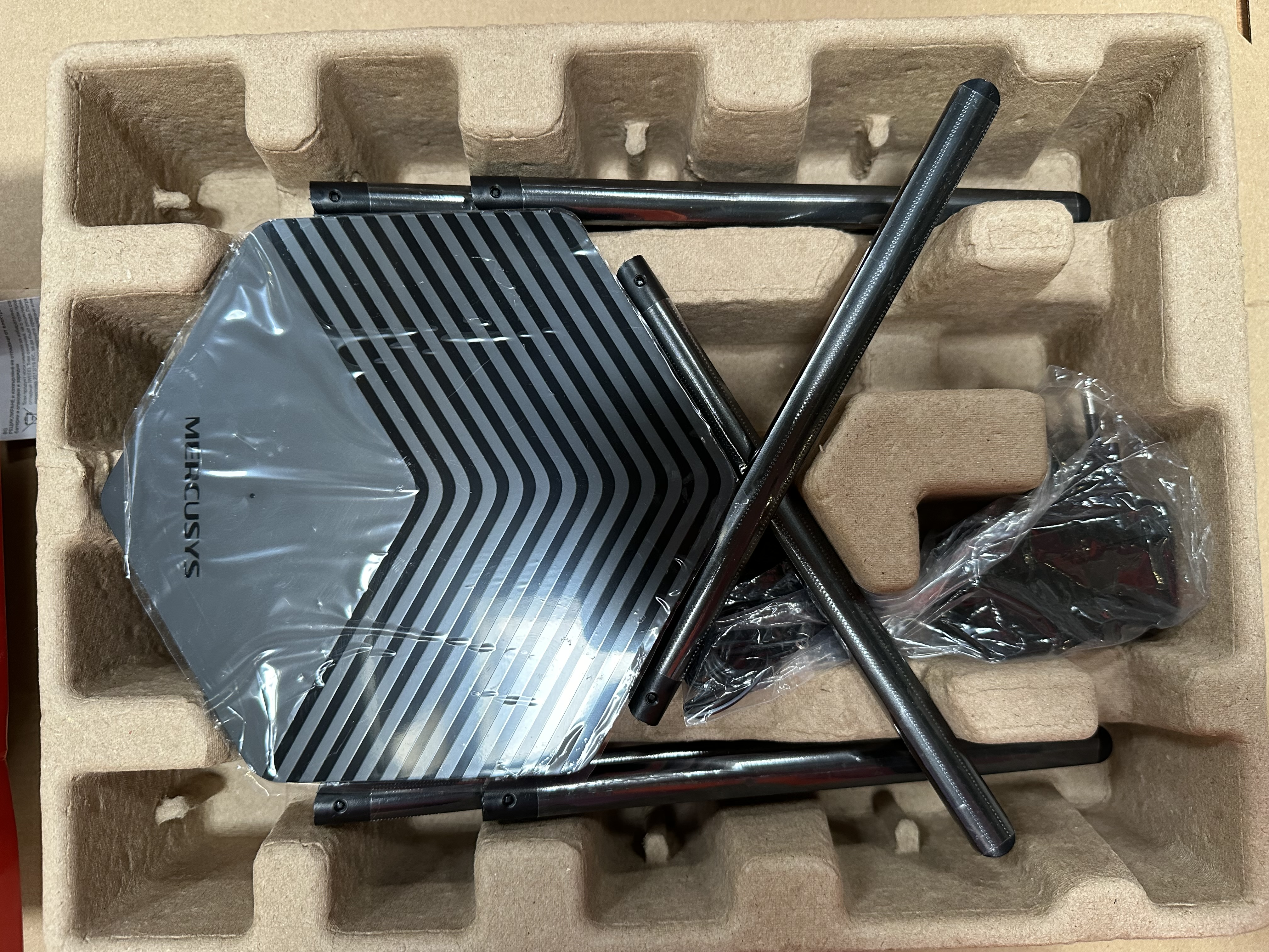 Zestaw routera w kartonie. Niektóre części są widoczne, zapakowane w plastik.