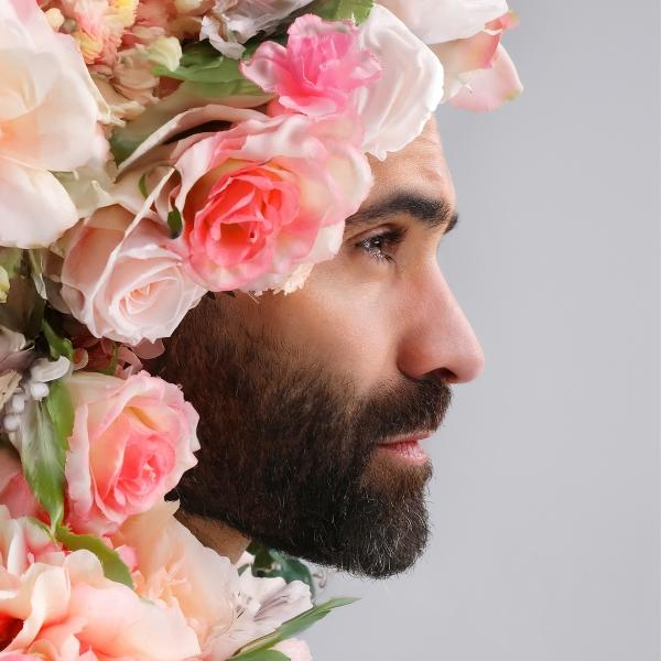 Un homme barbu de profil, orné d'une couronne florale de roses roses et pêche.