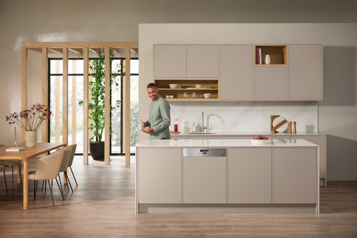 Eine moderne Küche mit Mann, Kücheninsel, Schränken und großem Fenster mit Tageslicht.