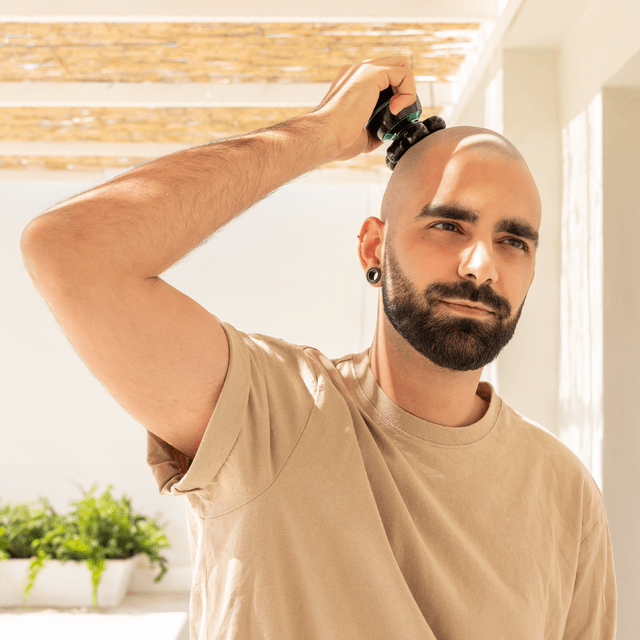 Mężczyzna goli głowę maszynką elektryczną, patrząc w górę.