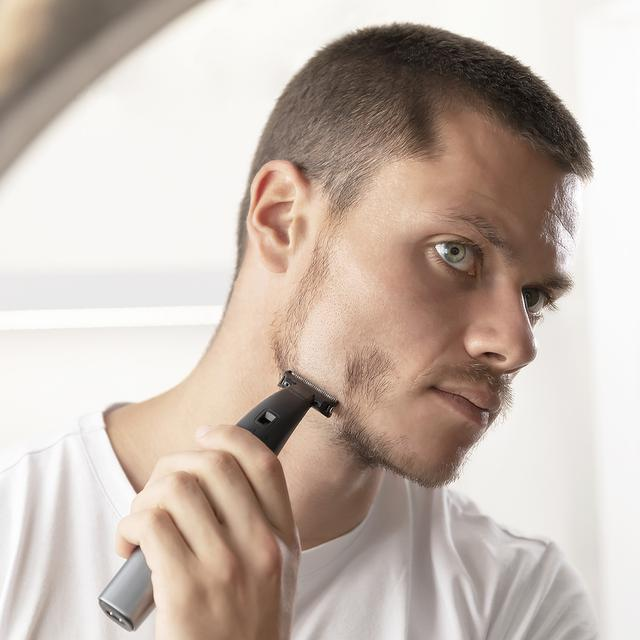 Mężczyzna przycina zarost czarną, elektryczną maszynką.