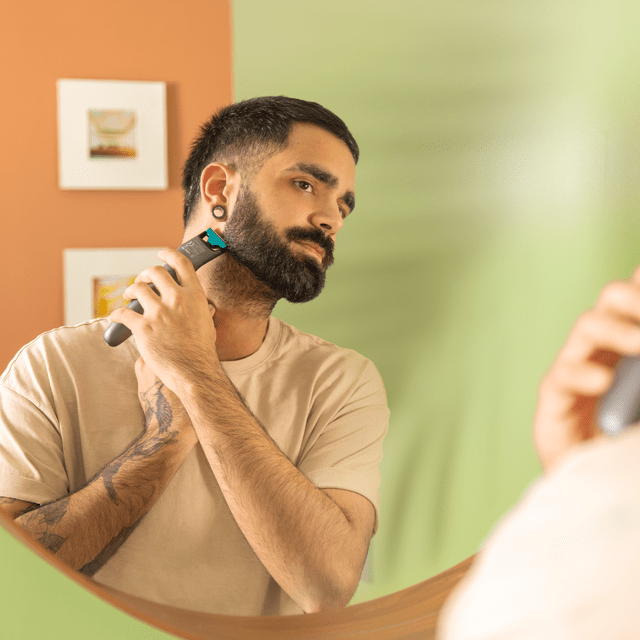 Mężczyzna przycina brodę trymerem przed lustrem.