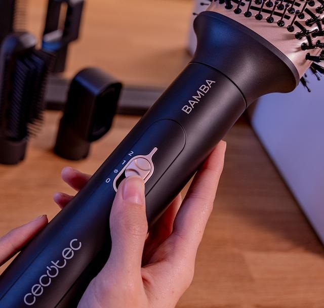 Zbliżenie osoby trzymającej szczotkę do suszarki. Suszarka jest czarna z różowymi akcentami. Tło jest rozmyte.