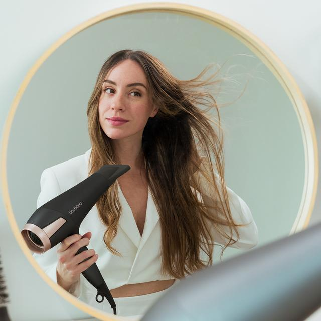 Kobieta suszy włosy suszarką.