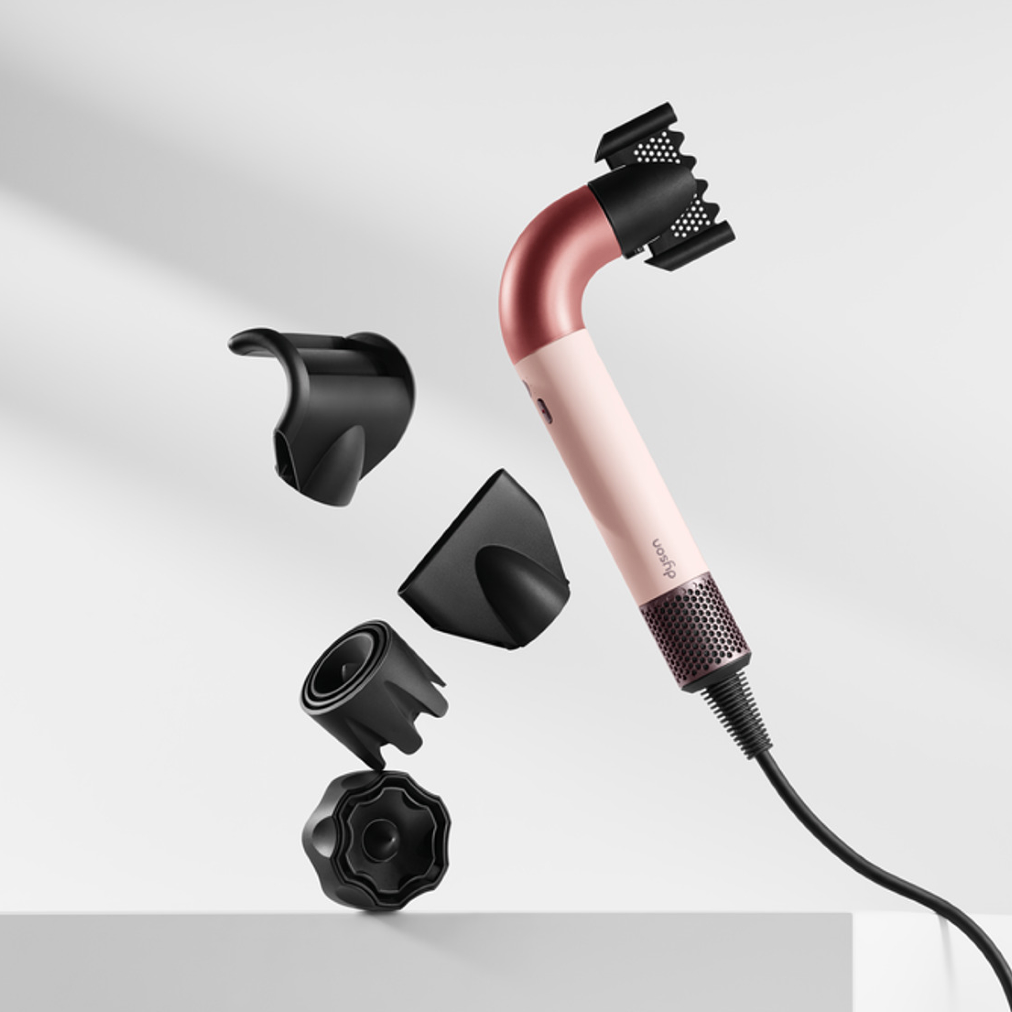 Haartrockner mit rosa Gehäuse und schwarzen Aufsätzen. Verschiedene Düsen werden angezeigt.