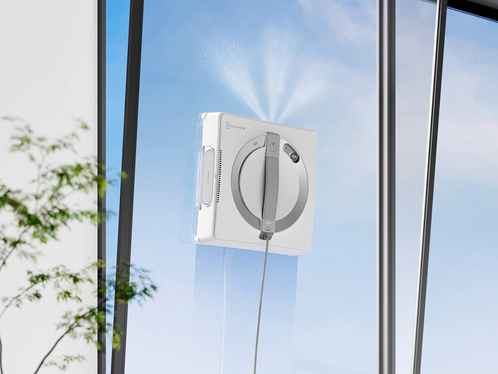 Biały robot do czyszczenia okien spryskujący wodą i czyszczący szkło, z niebieskim niebem w tle.