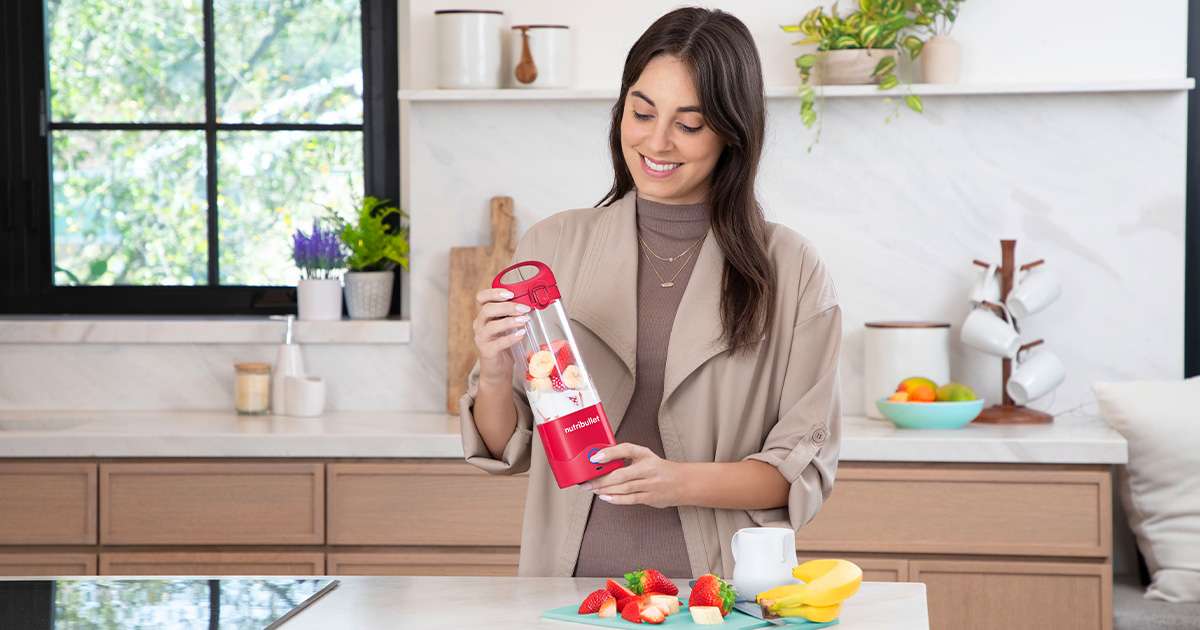 Frau hält Mixer, Küchenszene mit Obst.