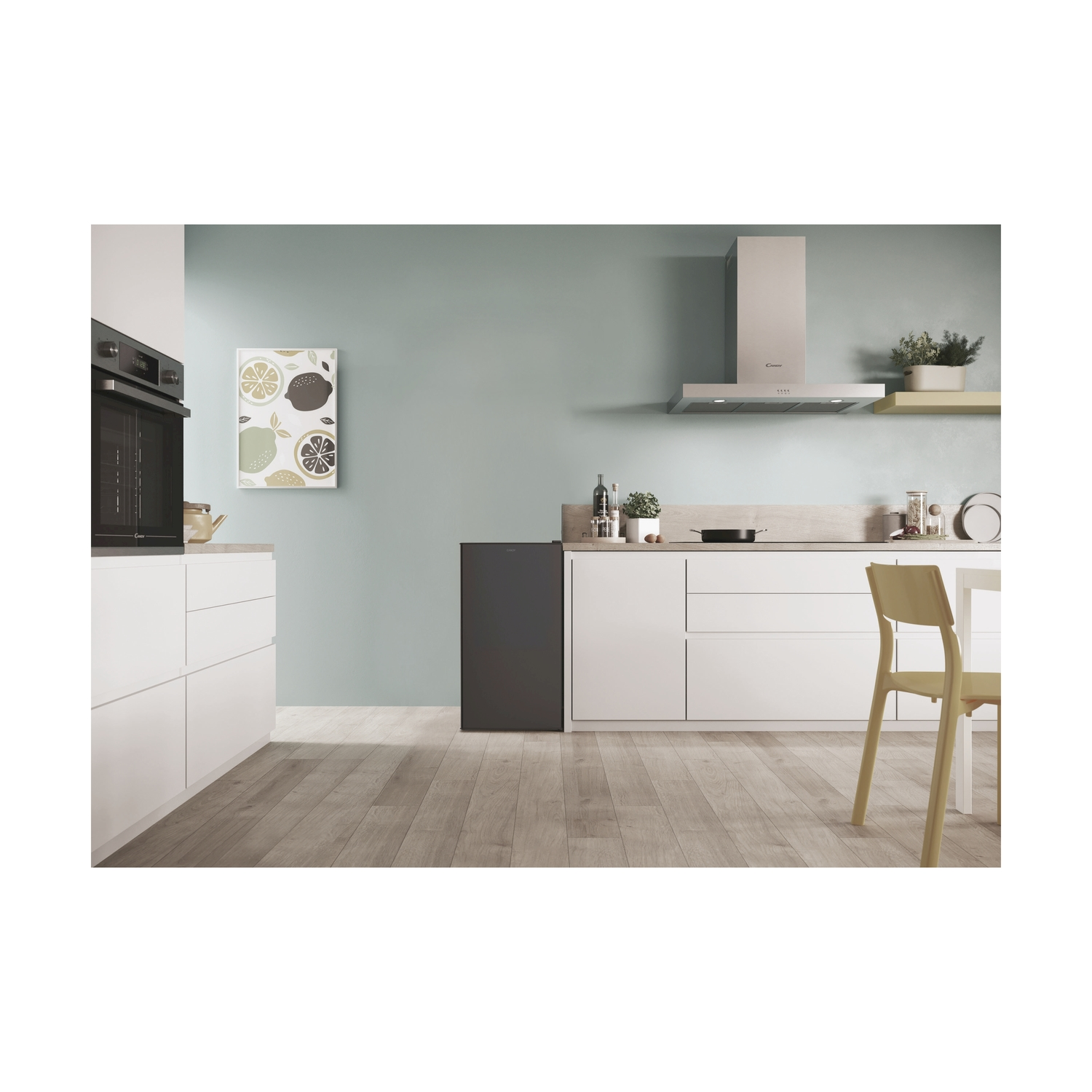 Interno cucina con un piccolo frigorifero nero. Visibili mobili bianchi, pavimenti in legno e una parete verde menta.