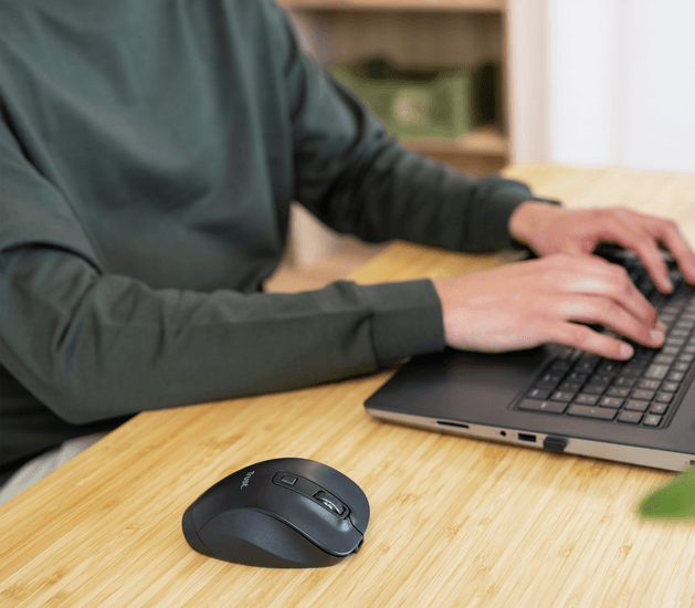 Egy személy laptopon gépel, fekete egérrel egy fa asztalon. Zöld doboz a háttérben.