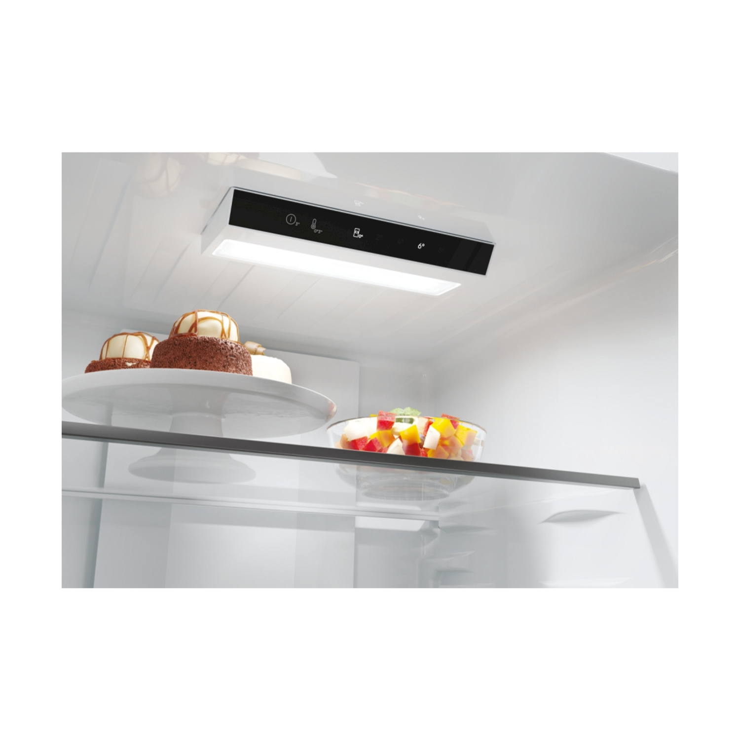 All'interno di un frigorifero, una luce illumina i ripiani con generi alimentari, tra cui torte e frutta.