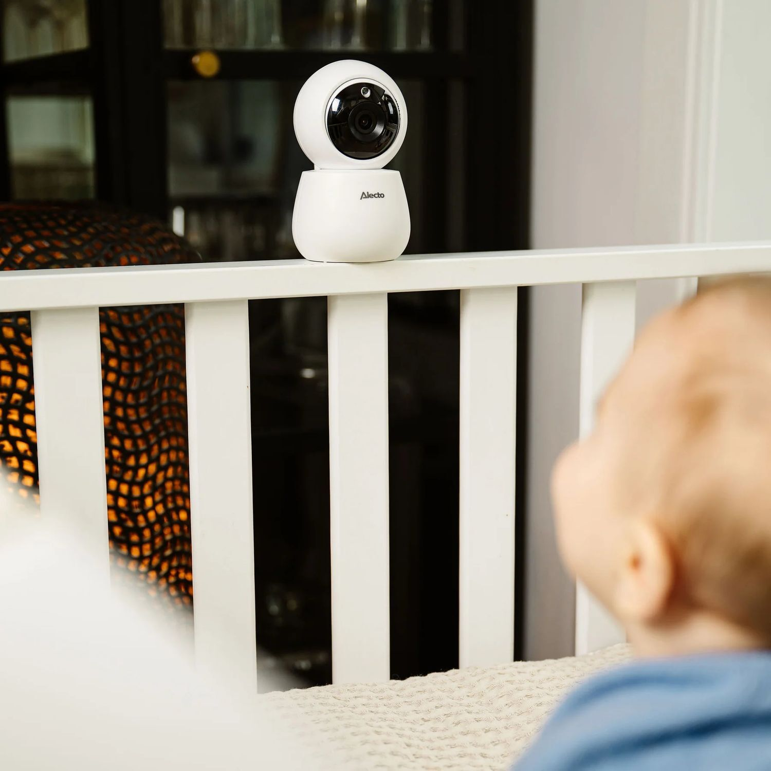 Un babyphone blanc sur un berceau, visage de bébé au premier plan.
