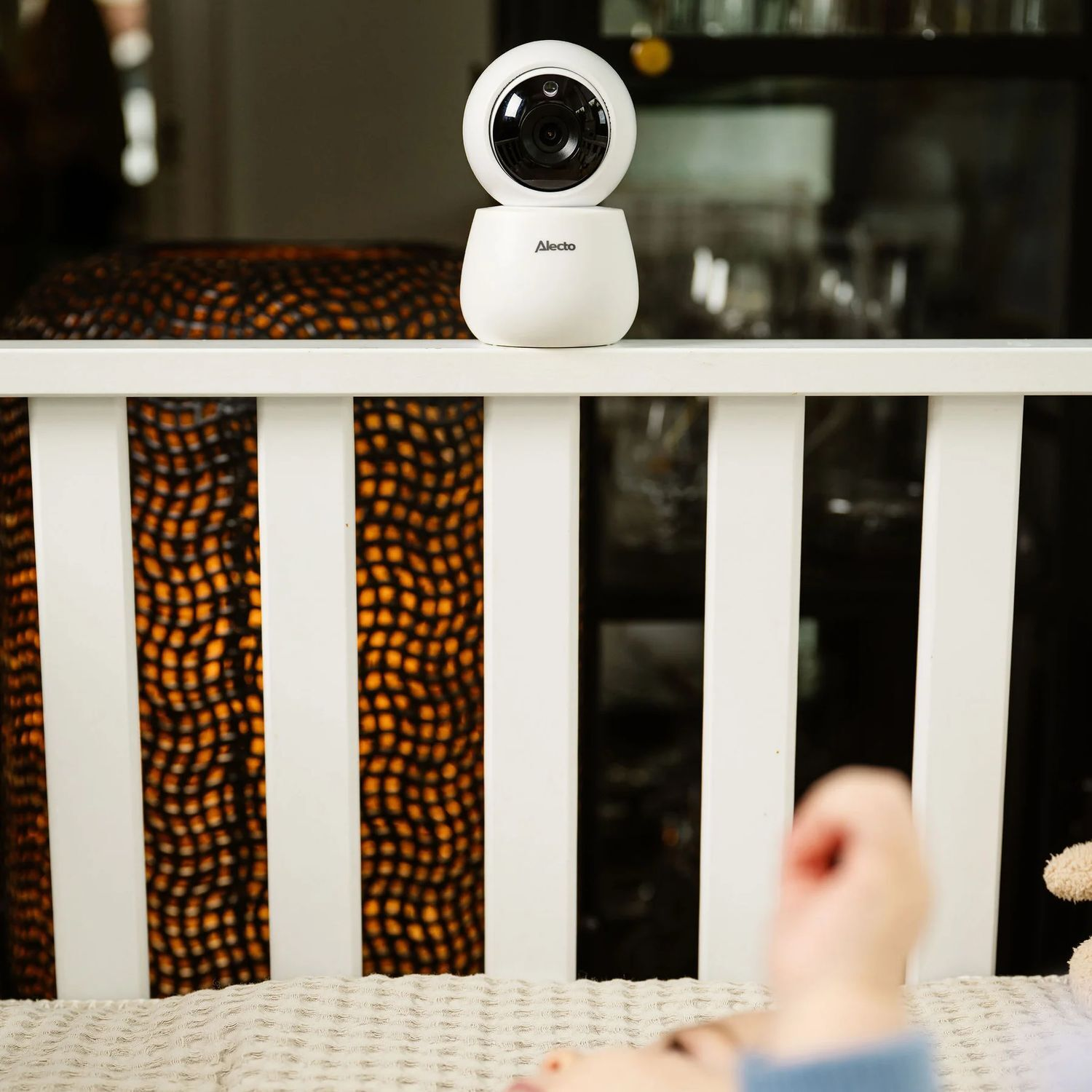 Babyphone blanc sur un berceau avec un bras d'enfant visible. Éclairage chaleureux.