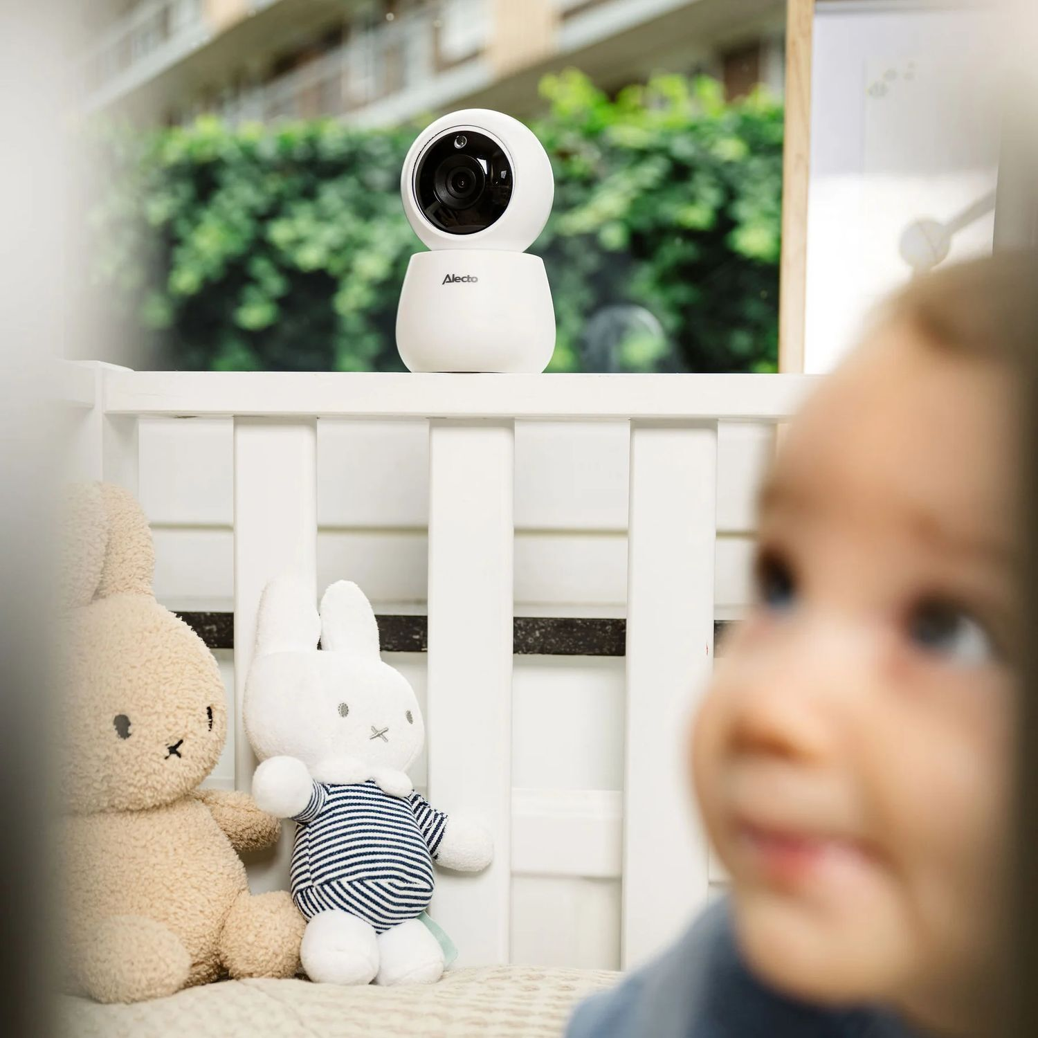 Un babyphone blanc sur un berceau. Un bébé est visible au premier plan.