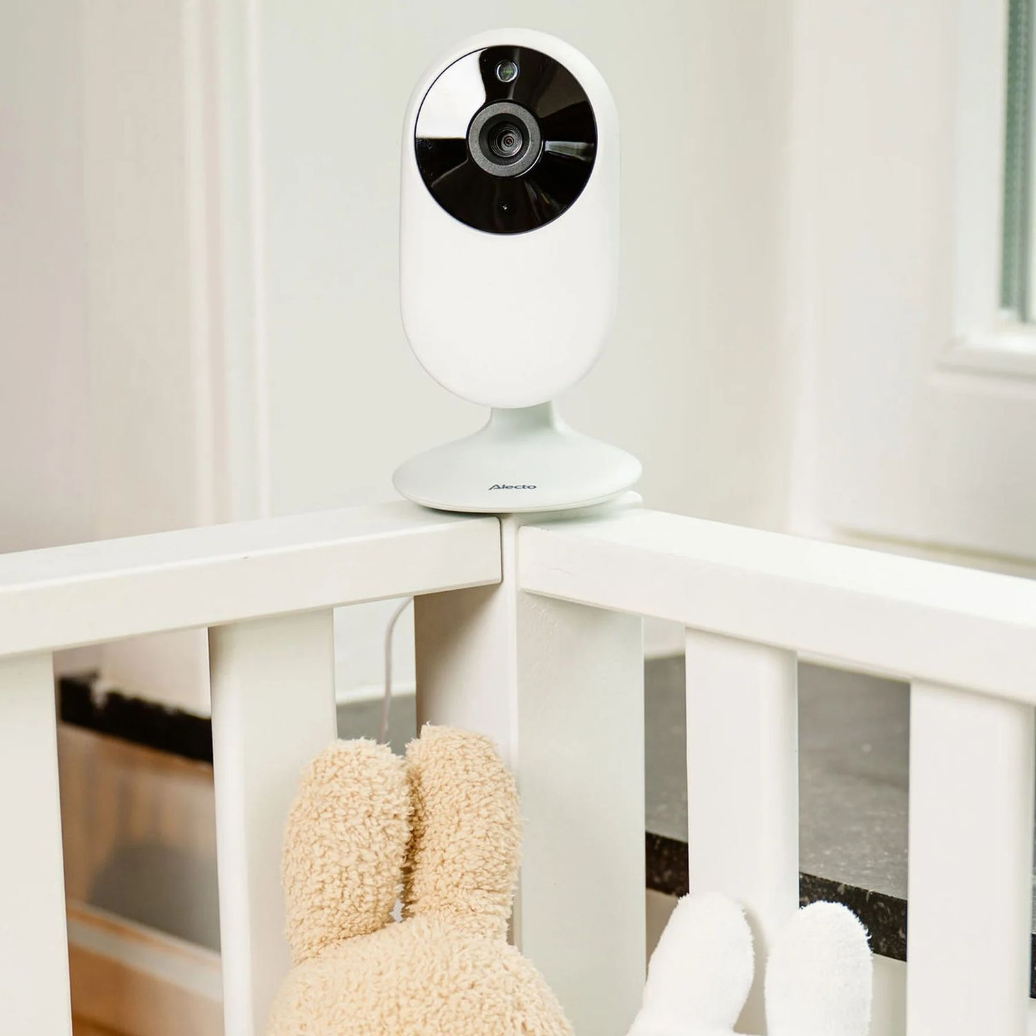 White baby monitor camera on a crib. Shows the camera, crib, and a plush toy.