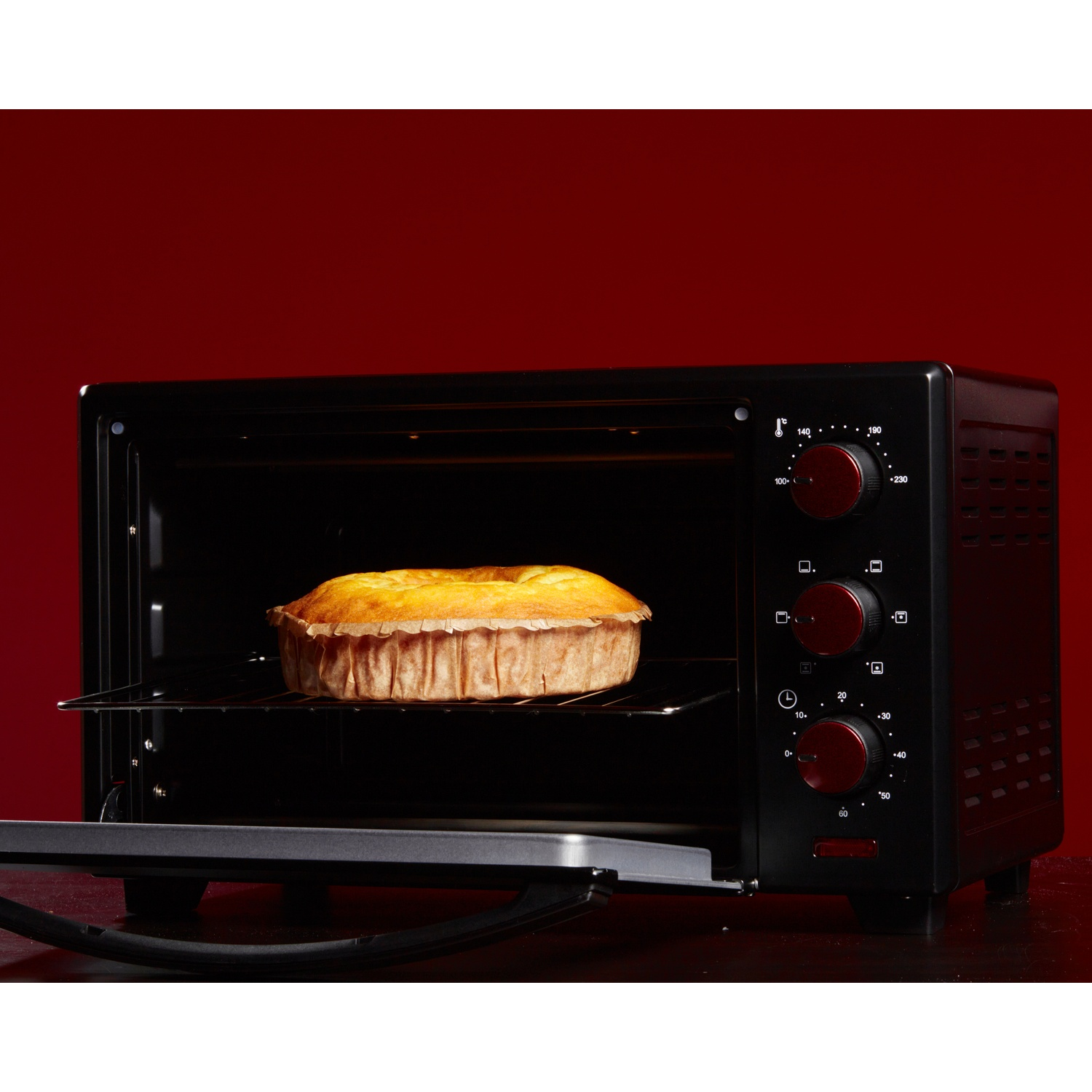 Forno nero con torta cotta dentro. Porta aperta, contro parete rossa.