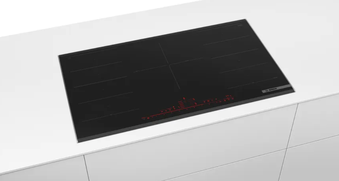 Placa de cocina negra sobre encimera blanca. Tiene cuatro zonas de cocción.