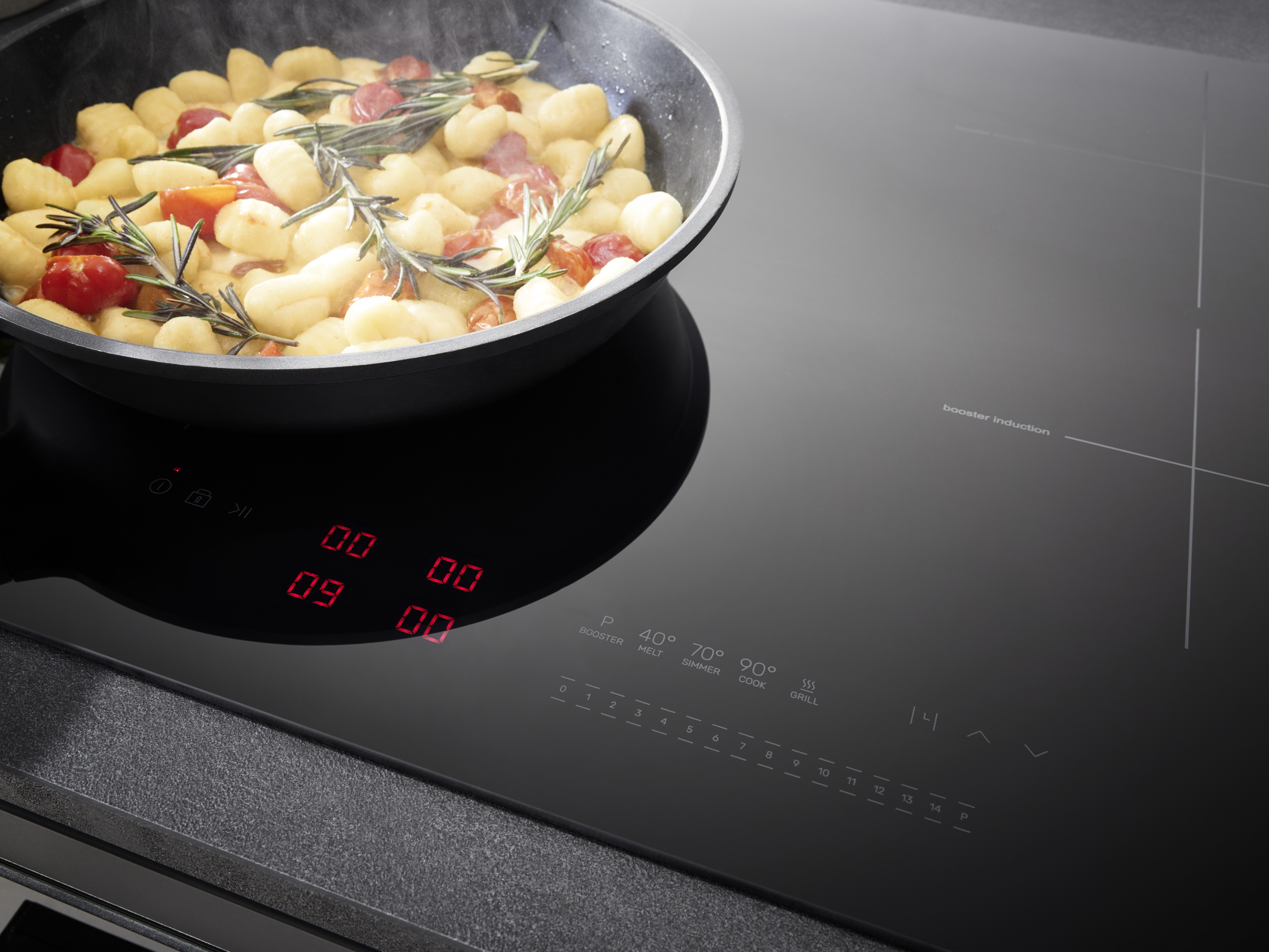 Pfanne mit Gnocchi, Tomaten und Rosmarin auf einem schwarzen Induktionskochfeld.