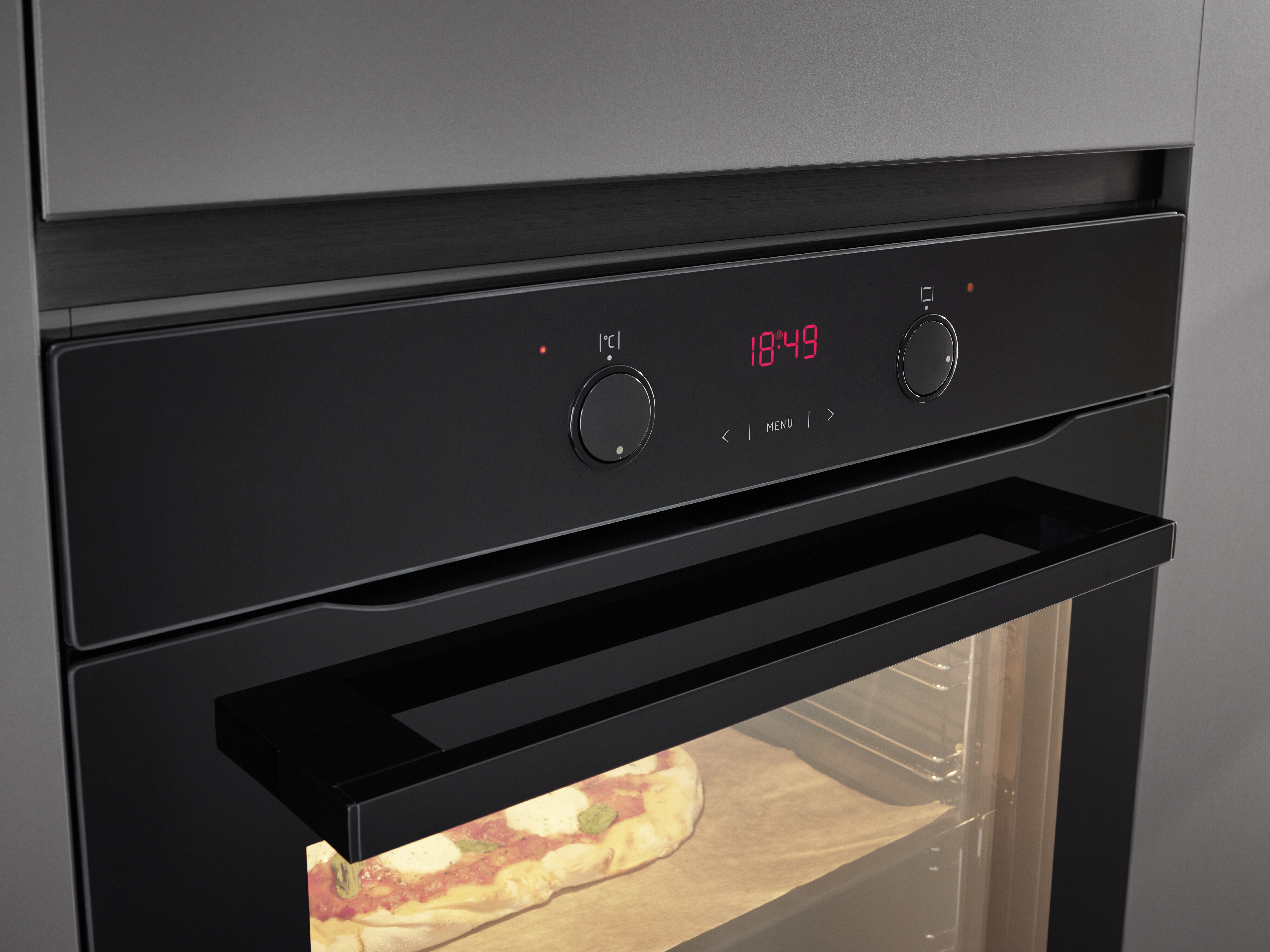 Schwarzer Backofen mit Digitalanzeige, Pizza sichtbar. Zwei Knöpfe oben.
