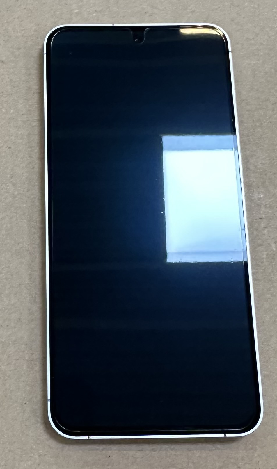 Czarny smartfon z białą ramką, na beżowej powierzchni.