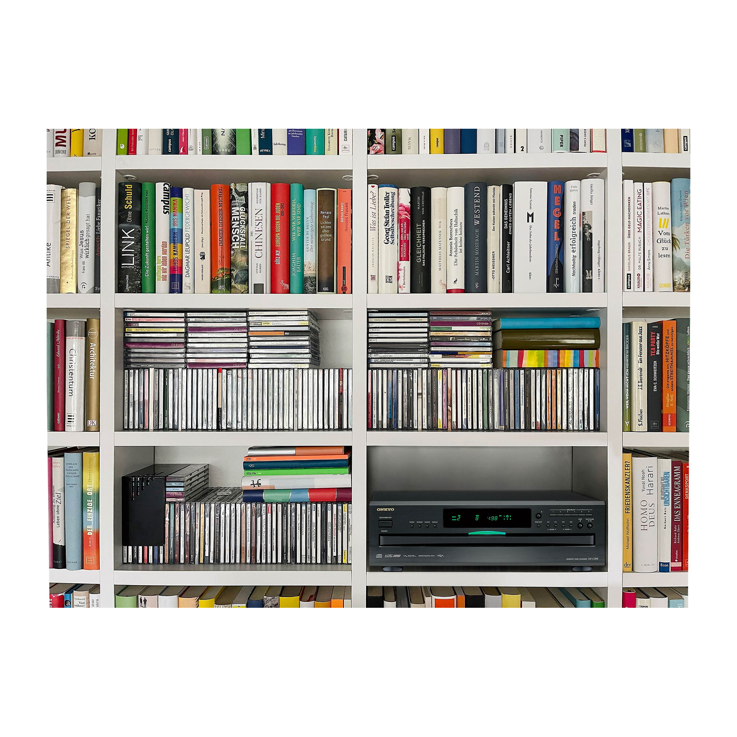 Een witte boekenkast vol boeken en cd's. In het midden staat een cd-speler.