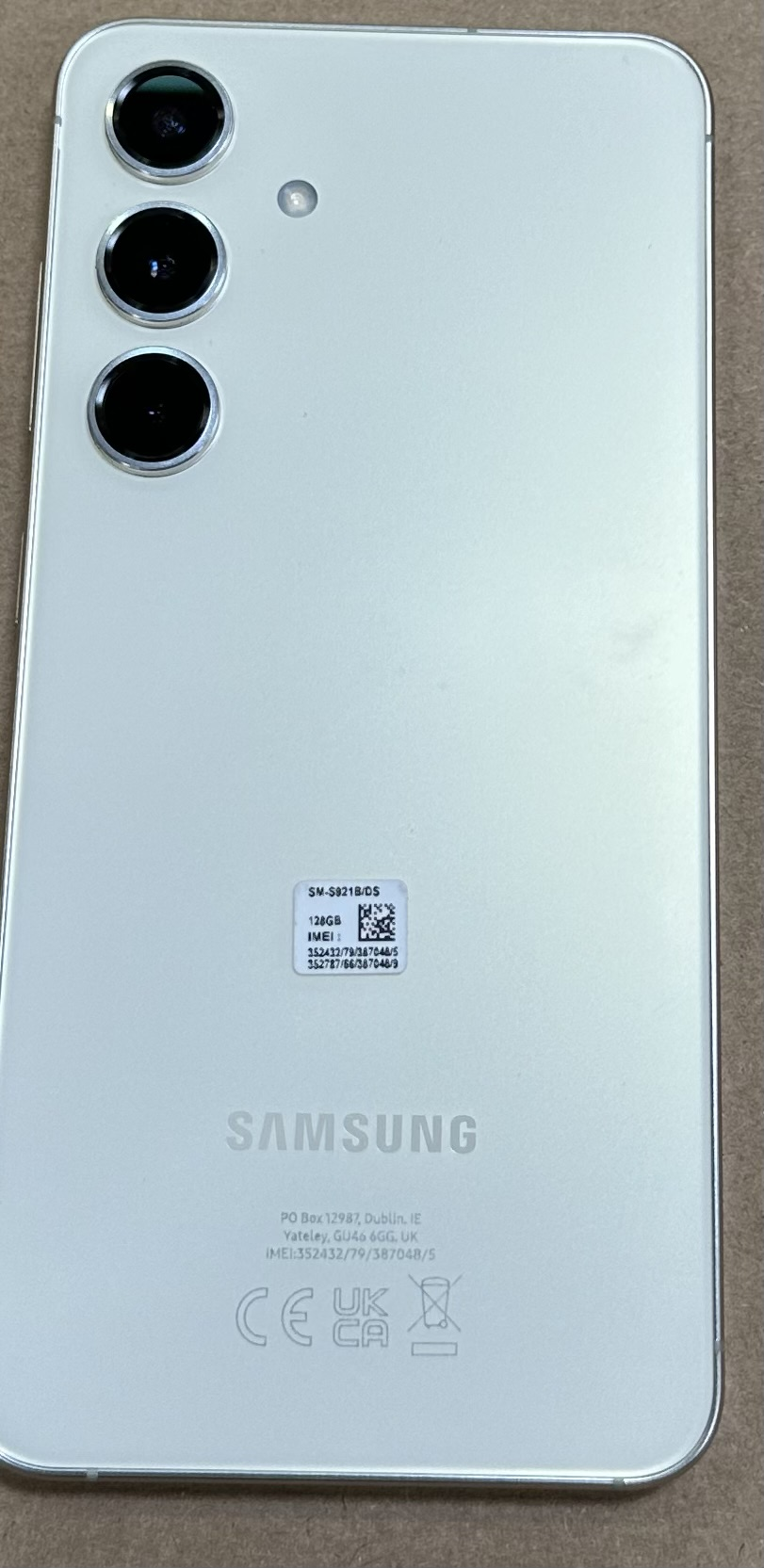 Tył białego smartfona z potrójnym aparatem i marką Samsung.