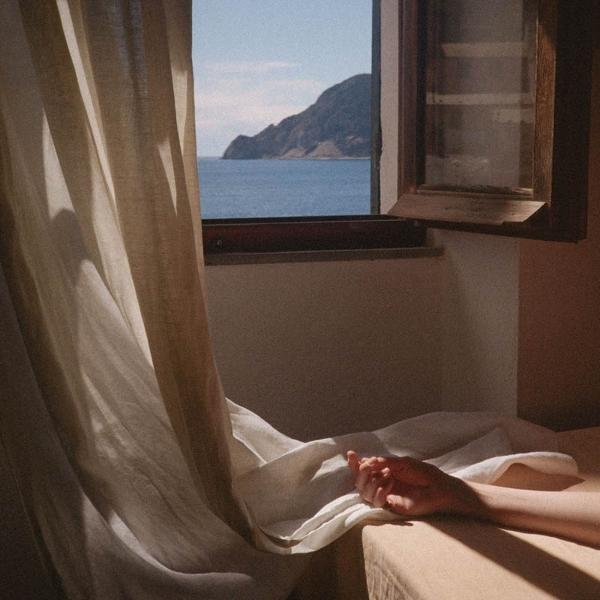 Hand auf Bett. Fenster mit Meerblick.
