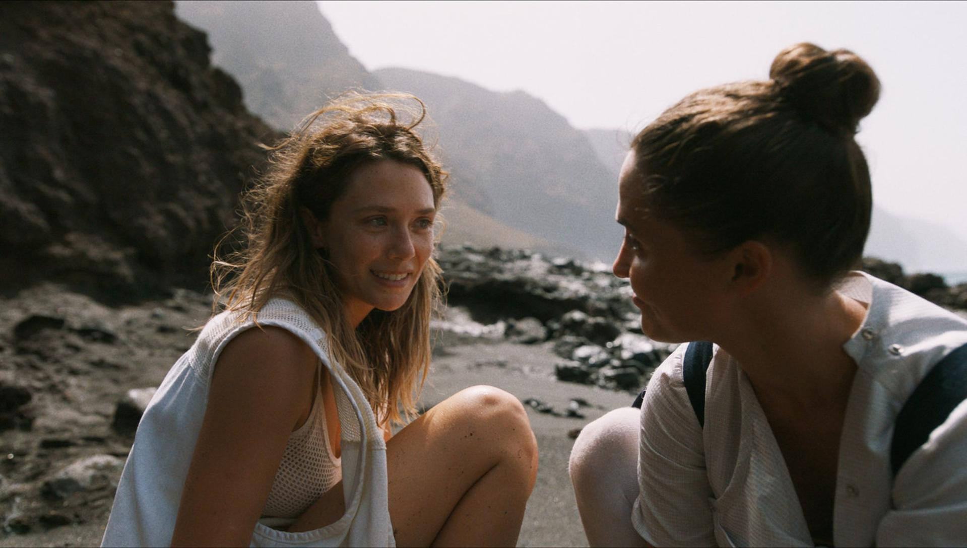Zwei Frauen an einem dunklen Strand, die sich in einer Nahaufnahme anlächeln.