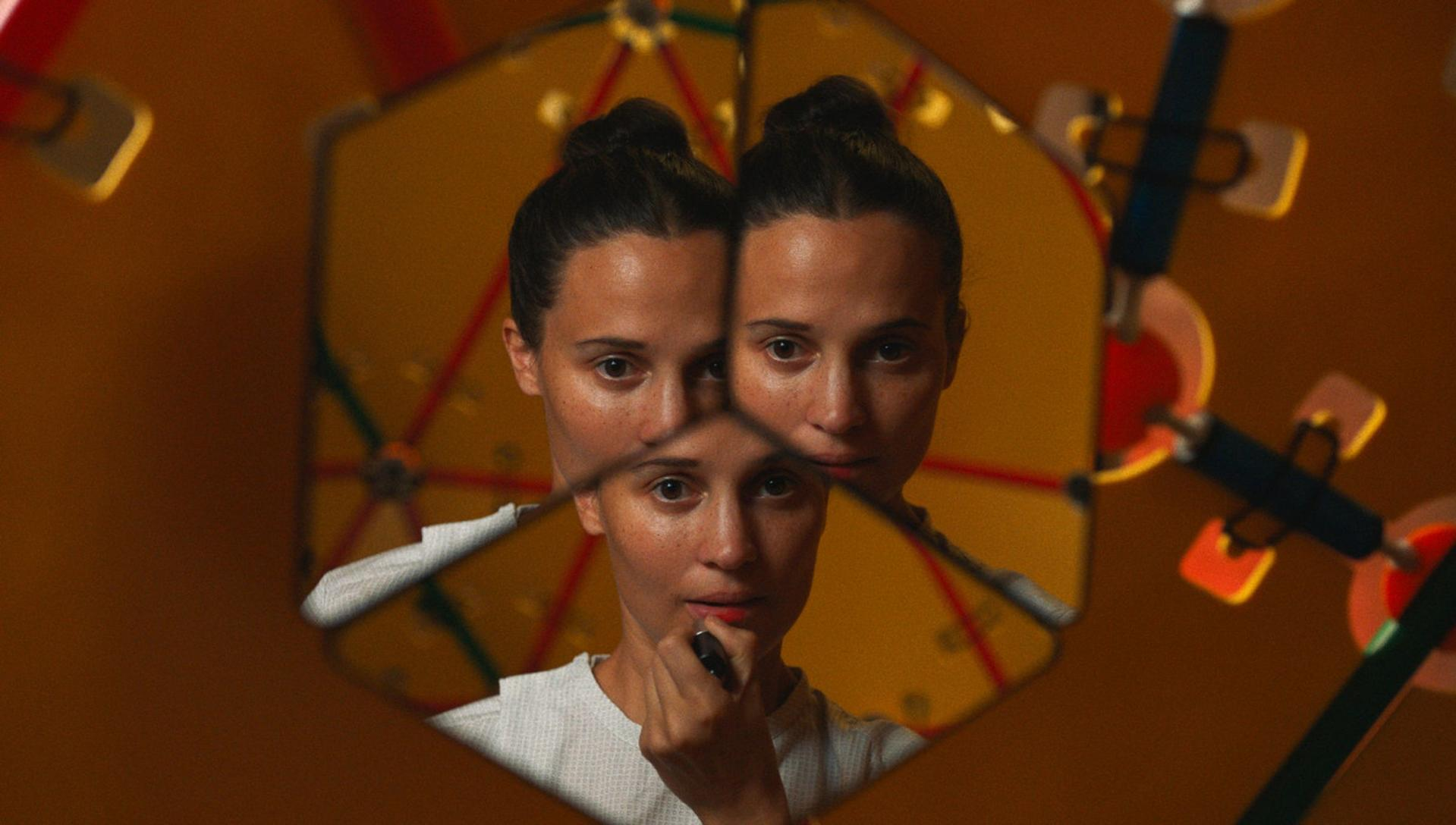 Eine Frau, die Lippenstift aufträgt, reflektiert in einem Kaleidoskop, mit orange-gelbem Hintergrund.