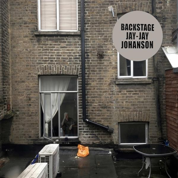 Ansicht eines Backsteingebäudes und einer Gasse. Eine Person schaut aus einem Fenster. Logo in einem Kreis oben.
