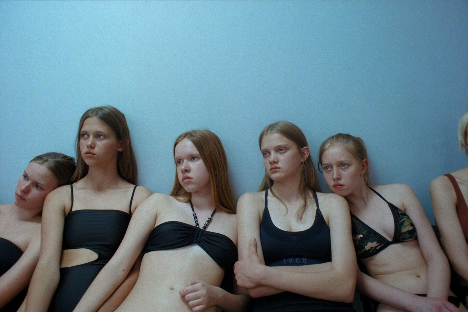 Gruppe junger Frauen in Badeanzügen, die vor einer blauen Wand sitzen.