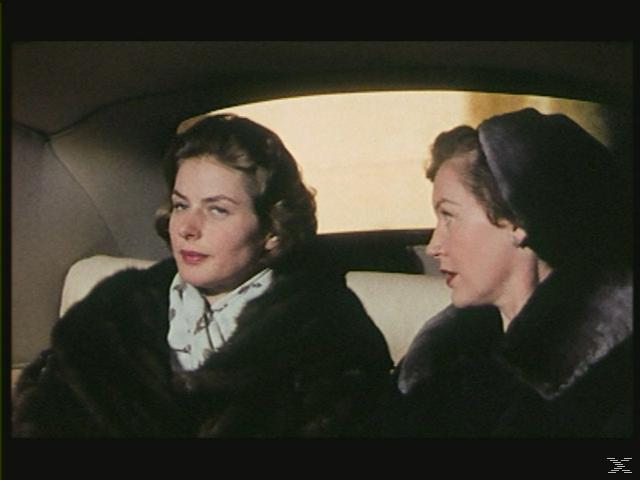 Zwei Frauen in einem Auto, eine mit Pelzmantel nach vorne schauend, die andere mit Hut zur Seite blickend.